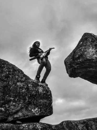 woman playing electric guitar on top of rock formation